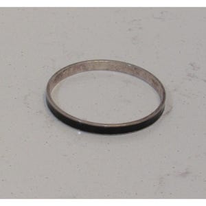 May include: A silver bangle bracelet with a black enamel inlay. The bracelet is circular and sits on a white surface. The jewelry piece is simple and elegant.