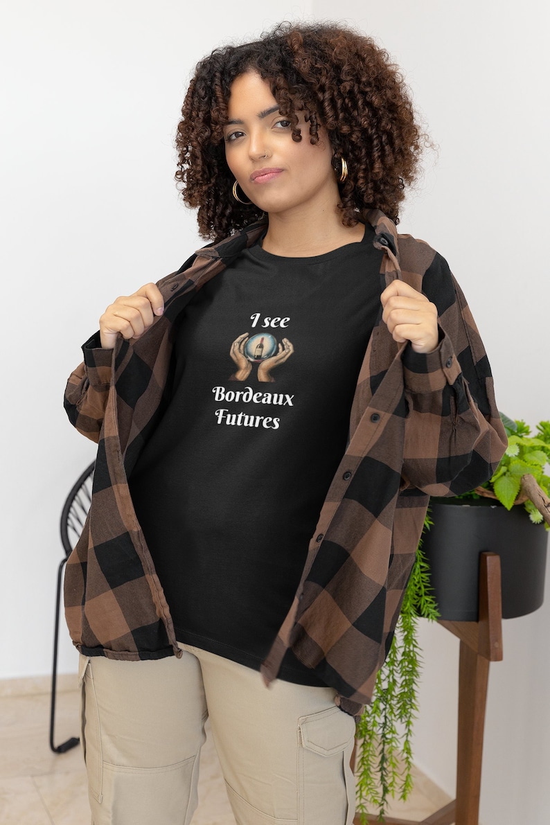 Peut inclure: Un t-shirt noir avec un motif blanc d'une main tenant une boule de cristal avec une bouteille de vin &agrave; l'int&eacute;rieur. Le texte "I see Bordeaux Futures" est imprim&eacute; sous le motif.
