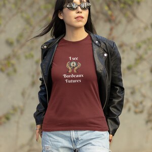 Peut inclure: Un t-shirt bordeaux avec un graphique d'une main tenant une boule de cristal avec une bouteille de vin &agrave; l'int&eacute;rieur. Le texte "I see Bordeaux Futures" est imprim&eacute; sous le graphique.