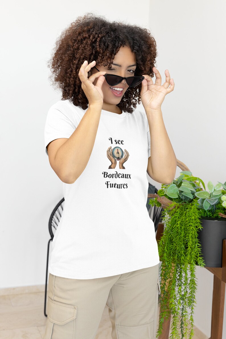 Peut inclure: T-shirt blanc avec un graphique d'une boule de cristal avec des mains la tenant. Le texte sur le t-shirt est "I see Bordeaux Futures".