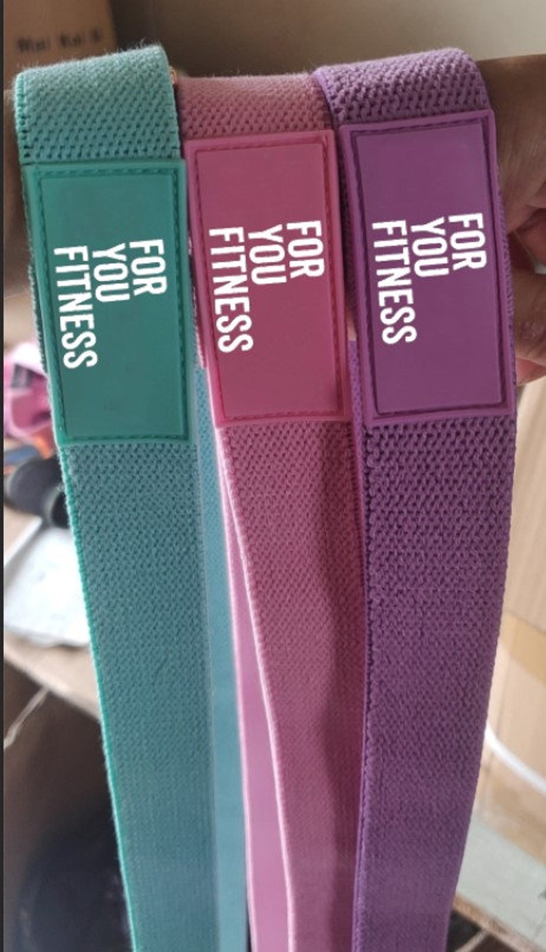 Pode incluir: Tr&ecirc;s bandas de resist&ecirc;ncia de tecido em verde, rosa e roxo com o texto "FOR YOU FITNESS" impresso em cada banda.