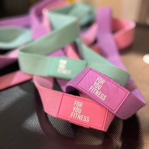 Pode incluir: Um conjunto de faixas de resist&ecirc;ncia em rosa, roxo e verde com o texto "For You Fitness" impresso nas faixas.