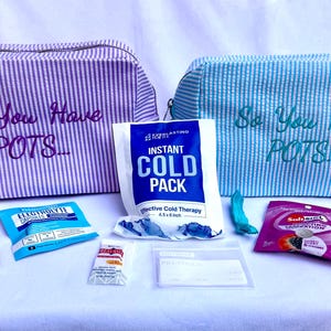 May include: Two zippered pouches with purple and blue stripes, each embroidered with the text So You Have POTS. The set includes an instant cold pack, a bottle of rescue drops, various electrolyte packets, a snack bar, and an I HAVE POTS card.