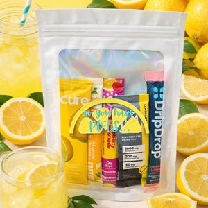 Puede incluir: Una bolsa blanca con una ventana transparente que muestra paquetes de mezcla de bebidas electrolíticas, limones y un vaso de limonada. Los paquetes son amarillos, rosas y azules. El texto "so you have POTS" es visible.