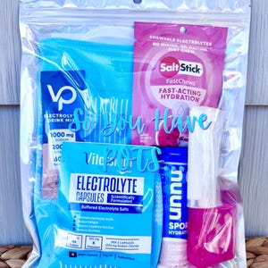 Könnte beinhalten: Ein transparenter holografischer Beutel mit verschiedenen Elektrolytprodukten, darunter eine blaue Kompressionsmanschette, eine rosa SaltStick FastChews-Packung, eine blaue Vitassium-Elektrolytkapsel-Packung, eine Nuun Sport-Tube und ein rosa Lippenbalsam.