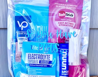 May include: A clear holographic pouch containing various electrolyte products including a blue compression sleeve, a pink SaltStick FastChews packet, a blue Vitassium electrolyte capsule packet, a Nuun Sport tube, and a pink lip balm container.
