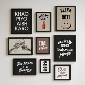 May include: Nine framed art prints with different text-based designs. The prints include phrases such as "Chai o'clock" and "This kitchen is for Dancing." The frames are black, and the backgrounds vary in colour. The prints are hung on a white wall.