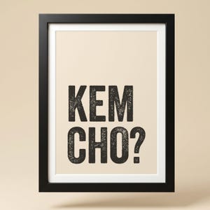 Peut inclure: Une affiche murale rectangulaire dans un cadre noir présentant le texte KEM CHO? en lettres capitales noires, grasses et texturées, centrées sur un fond beige clair. L'affiche est entourée d'un passe-partout blanc dans le cadre noir.