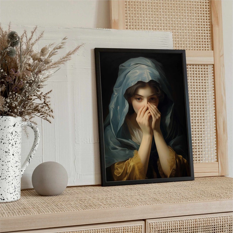 May include: A framed painting of a woman in a blue hooded robe, with her hands covering her face. The woman's expression is one of sadness or contemplation. The painting is set against a dark background.