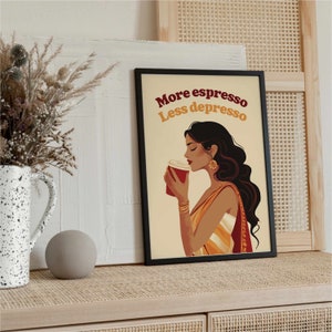 May include: A framed wall art print featuring an illustration of a person with long dark hair holding a red coffee cup. The text "More espresso Less depresso" is printed in dark red and yellow above the figure, who wears gold jewelry.