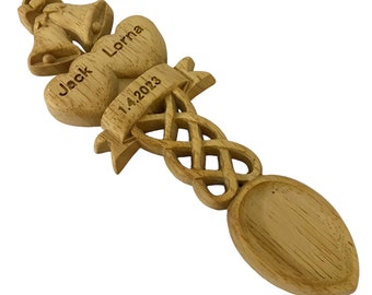 May include: A carved wooden love spoon. The spoon has two bells, two hearts with the names "Jack" and "Lorna", and a banner with the date "1.4.2023". The handle features a Celtic knot design. The spoon is made of light-colored wood.