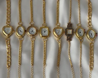 May include: Eight gold-tone wristwatches with chain-link bracelets arranged in a row. The watches feature various case shapes including heart, oval, round, and square, all with white dials, black numerals, and gold-tone hands and markers.