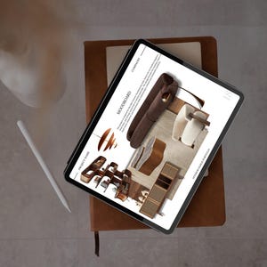 May include: A digital tablet displaying a mood board for an interior design portfolio. The tablet rests on a brown leather-bound notebook, with a white stylus and a white object in the background. The mood board features furniture and design elements.