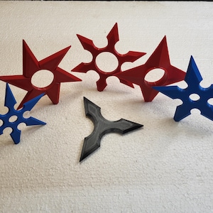 May include: Five different throwing stars, also known as shurikens, in various colours. Two are red, one is blue, and two are black.