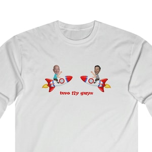 May include: White long-sleeve shirt featuring a graphic of two cartoon men riding red and white rockets. The text "two fly guys" is printed below the rockets in red. The shirt has a crew neck and long sleeves.