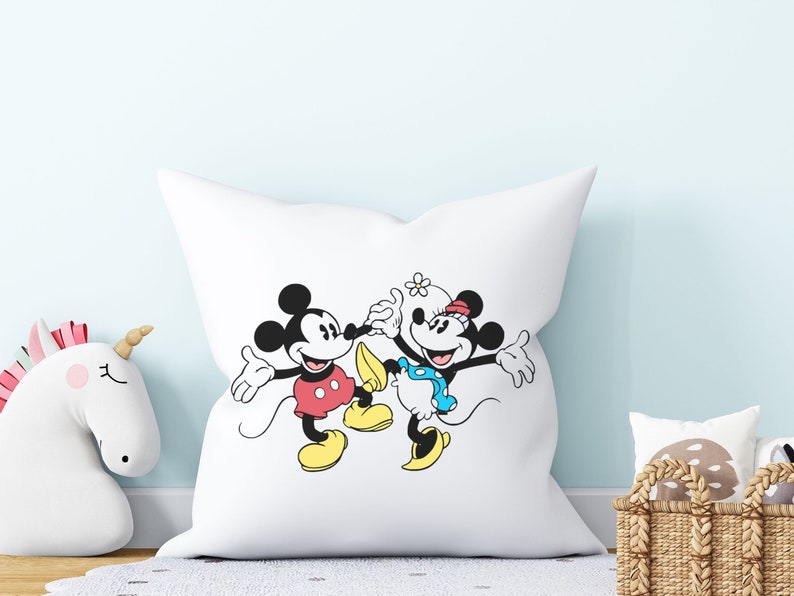 Puede incluir: Almohada blanca con una ilustraci&oacute;n en blanco y negro de Mickey Mouse y Minnie Mouse. Mickey lleva pantalones cortos rojos y zapatos amarillos. Minnie lleva un vestido de lunares azules y blancos y zapatos amarillos.