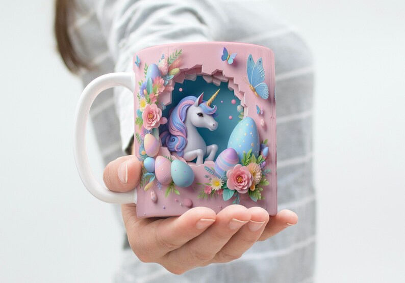 May include: A pink ceramic mug with a 3D design featuring a white unicorn with a blue and pink mane and tail, surrounded by pastel-colored Easter eggs and flowers. The unicorn is peeking out of a hole in the mug.