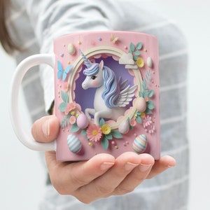 May include: A pink ceramic mug with a white handle features a 3D papercraft design of a unicorn with pastel blue and purple accents. The unicorn is surrounded by flowers and pastel-colored Easter eggs.