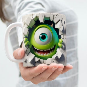 May include: A white ceramic mug with a green monster character breaking through a cracked wall design. The monster has one large eye and a toothy grin.