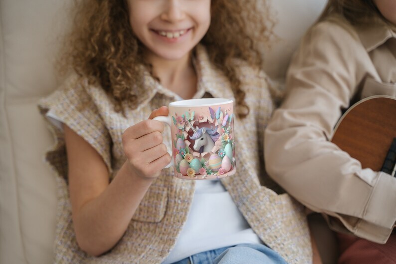May include: A white ceramic mug with a colorful design featuring a unicorn peeking out of an Easter egg. The mug is surrounded by pastel-colored eggs and flowers.