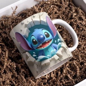 May include: A white ceramic mug with a 3D image of Stitch, a blue alien character from the Disney movie Lilo & Stitch, breaking through the mug. Stitch is smiling and has his signature blue eyes and large ears. The mug is surrounded by brown packing peanuts.