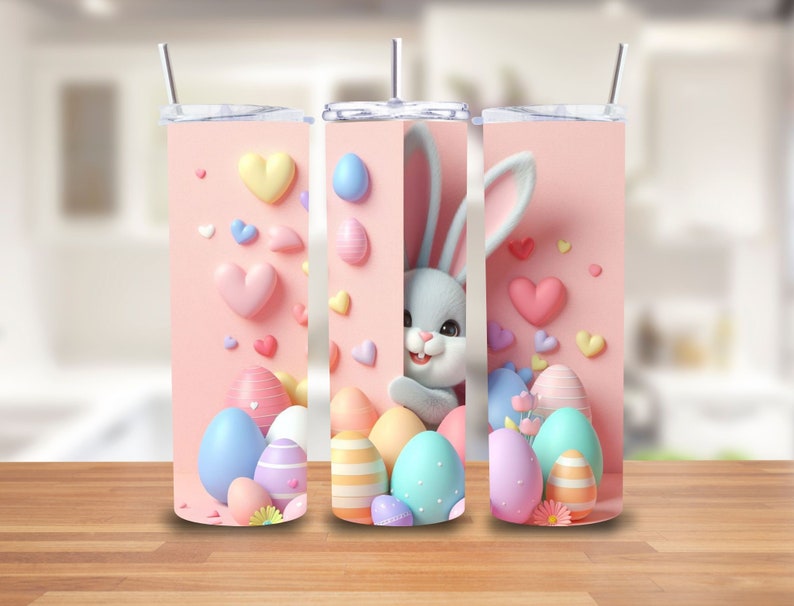 Puede incluir: Tres vasos t&eacute;rmicos rosas y blancos con un tema de Pascua pastel. Cada vaso presenta un conejito de dibujos animados, corazones y huevos coloridos.