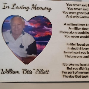 May include: A white wooden plaque with a heart-shaped cutout featuring a photo of a man. The plaque has a poem inscribed on it that reads "In Loving Memory William "Otis" Elliott You never said I'm leaving You never said goodbye. You were gone before I knew it And only God knows why. A million times I needed you. A million times I cried. If love alone could have saved you, You never would have died. In life I loved you dearly. In death I love you still. In my heart you hold a place That no one could ever fill. It broke my heart to lose you. But you didn't go alone For part of me went with you. The day God took you home."