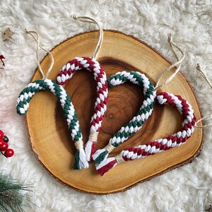 May include: Four handmade candy cane decorations, each with a white, red and green striped design. The decorations are made of braided yarn and have a loop for hanging.
