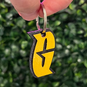 Puede incluir: Un llavero amarillo y negro con un diseño estilizado de la letra 'E'. El llavero está unido a un anillo de llave plateado.