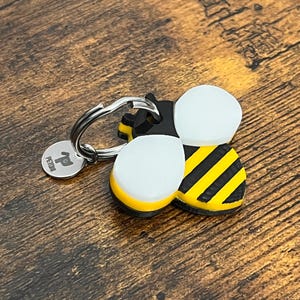 May include: A black and yellow bee-shaped keyring with a silver ring and a small silver tag that says "PETID".