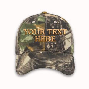 May include: A camouflage baseball cap with the text "YOUR TEXT HERE" embroidered in gold on the front.