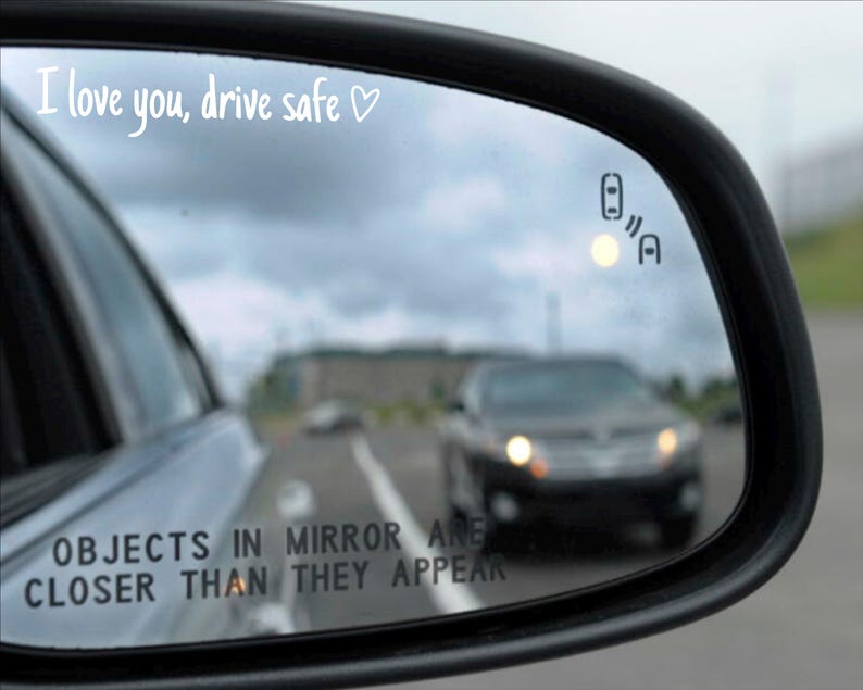 May include: A rearview mirror with the text "I love you, drive safe" written on it. The mirror is showing a car driving in the distance. The text "OBJECTS IN MIRROR ARE CLOSER THAN THEY APPEAR" is also visible on the mirror.