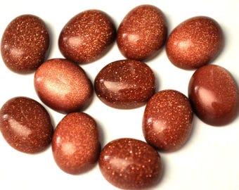 Puede incluir: Una colección de once gemas ovaladas y pulidas. Las piedras son de un color marrón rojizo intenso con un aspecto brillante y reluciente. Las gemas están dispuestas sobre una superficie blanca. Cada piedra mide unos 2-3 cm.