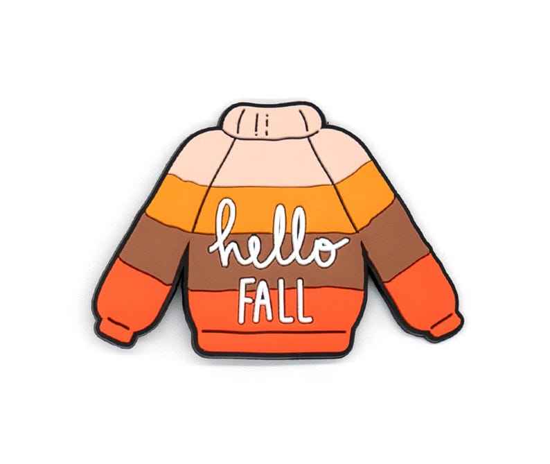 K&ouml;nnte beinhalten: Eine pulloverf&ouml;rmige Anstecknadel mit horizontalen Streifen in den Farben Hellrosa, Gelb, Braun und Orange. Der Text "hello FALL" ist in wei&szlig;er Schreib- und Blockschrift in der Mitte des kleidungsst&uuml;ckf&ouml;rmigen Accessoires zu sehen.