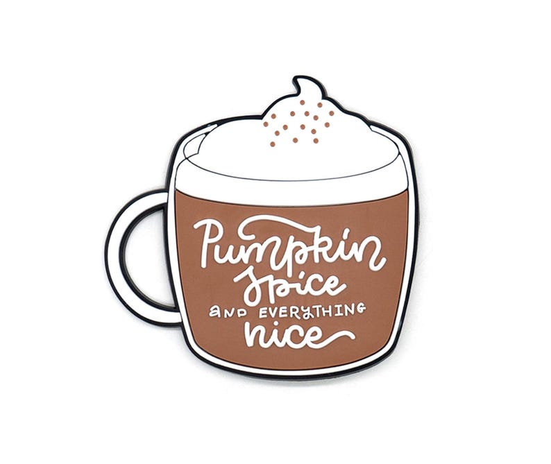 K&ouml;nnte beinhalten: Ein brauner Emaille-Pin in Form einer Kaffeetasse, gekr&ouml;nt von wei&szlig;er Schlagsahne und braunen Streuseln. Die Tasse zeigt den wei&szlig;en Schreibschrift-Text Pumpkin Spice and everything nice. Das Design ist schwarz umrandet und hat einen wei&szlig;en Henkel.