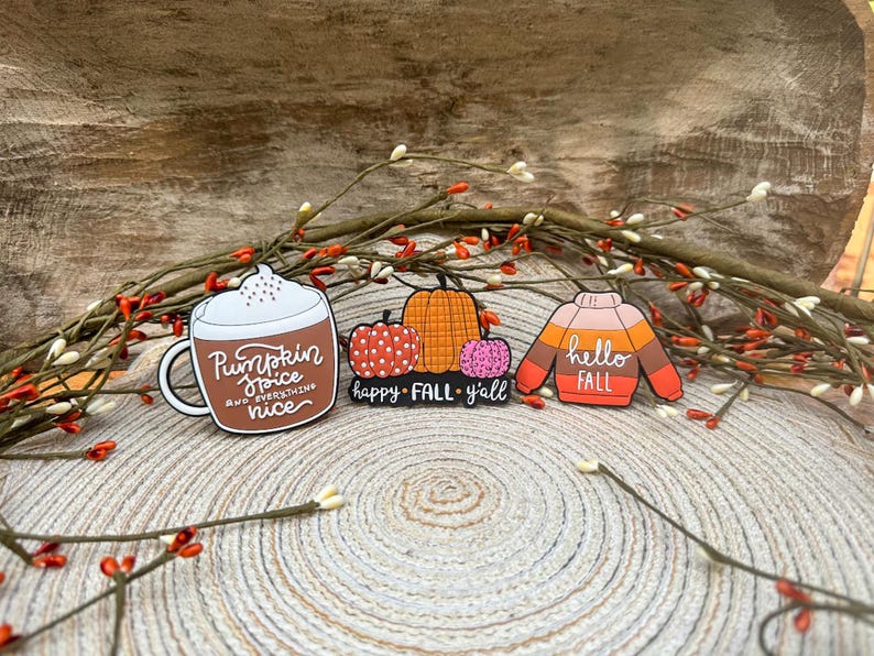K&ouml;nnte beinhalten: Drei Emaille-Anstecknadeln mit Herbstmotiven. Eine ist eine braune Tasse mit wei&szlig;em Schaum und dem Text Pumpkin Spice and everything nice. Eine weitere zeigt drei K&uuml;rbisse mit dem Text happy FALL y'all. Die dritte ist ein Pullover mit dem Text hello FALL.