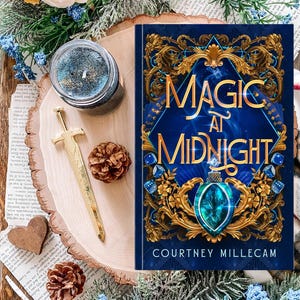 May include: A book titled "Magic at Midnight" with a blue cover and gold accents, a candle, a decorative sword, and a pinecone on a wooden surface. The book cover features the author's name, Courtney Millecam.