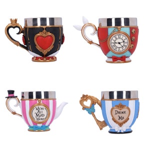 May include: Four ceramic teacups with different designs. The first cup is black with a red heart and gold accents. The second cup is red, white, and blue with a clock face and gold accents. The third cup is pink and white striped with gold accents and the text "We're All Mad Here". The fourth cup is blue and white striped with gold accents and the text "Drink Me".