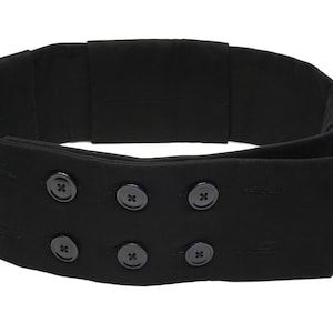 May include: A black fabric belt with a unique design featuring multiple buttons. The belt is folded over and has a pointed end.