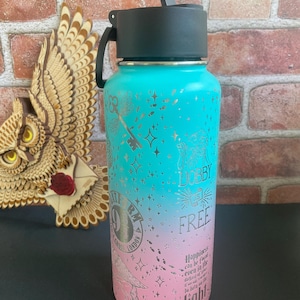 May include: A teal and pink water bottle with a black lid and handle. The bottle features silver illustrations of a key, stars, and text. The text includes the words "Lobby Free" and a quote about light.