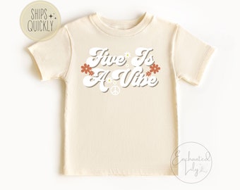 May include: A beige short-sleeved t-shirt with the text "Five Is A Vibe" in a retro font with flowers and a peace sign.