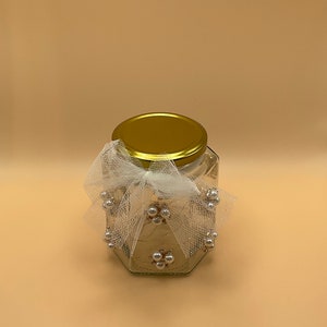 May include: A glass jar with a gold lid and a white tulle bow decorated with white pearl beads.