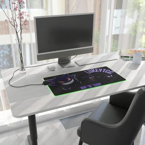 May include: A black and green gaming mouse pad with a purple and white graphic of a cartoon ghost. The mouse pad has the text "LUKEYTCG RIP 'N' SHIP" printed on it.