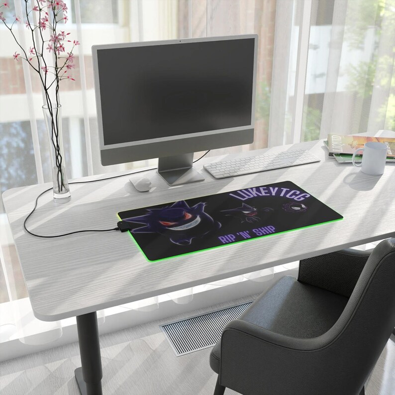 May include: A black and green gaming mouse pad with a purple and white graphic of a cartoon ghost. The mouse pad has the text "LUKEYTCG RIP 'N' SHIP" printed on it.