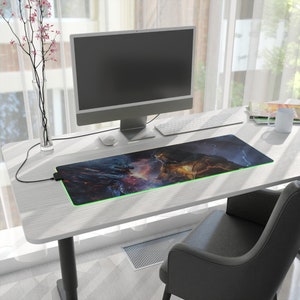 Centered prominently is a gaming desk mat, measuring 31.5 x 11.8, drawing attention to its impressive size. Adjacent to the mat, you'll find a sleek monitor, a cozy coffee cup, and a comfortable office chair, completing the inviting setup.