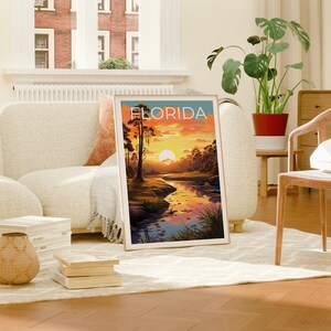 K&ouml;nnte beinhalten: Ein gerahmtes Poster mit einer Sonnenuntergangsszene &uuml;ber einem Fluss in einem Sumpf. Das Poster tr&auml;gt den Titel "FLORIDA" in wei&szlig;er Schrift.