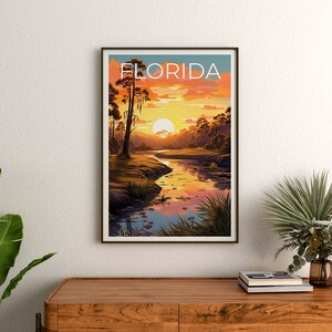 K&ouml;nnte beinhalten: Ein Vintage-Reiseposter mit einer Sonnenuntergangsszene &uuml;ber einem Fluss in Florida. Das Poster zeigt eine gro&szlig;e, orange Sonne, die hinter einer Baumreihe untergeht, und einen Fluss, der durch die Szene flie&szlig;t. Der Text "FLORIDA" ist in fetter, wei&szlig;er Schrift oben auf dem Poster gedruckt.