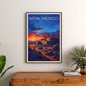 May include: A vintage travel poster featuring a sunset over a desert landscape with a pueblo-style building in the foreground. The poster is framed in a dark wood frame and has the text "NEW MEXICO" at the top.