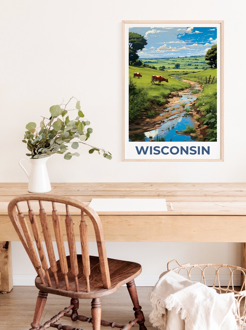 May include: A framed art print featuring a pastoral landscape with a stream, cows, and green fields under a blue sky. The word "WISCONSIN" is printed in navy blue at the bottom. The print is displayed on a wooden desk with a white vase and a wooden chair.