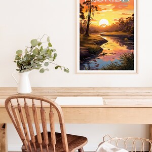 K&ouml;nnte beinhalten: Ein Vintage-Poster mit dem Wort "FLORIDA" in wei&szlig;er Schrift auf blauem Hintergrund. Das Poster zeigt einen Sonnenuntergang &uuml;ber einem Fluss in einem Sumpfgebiet mit hohen B&auml;umen und einer gro&szlig;en, orangen Sonne.